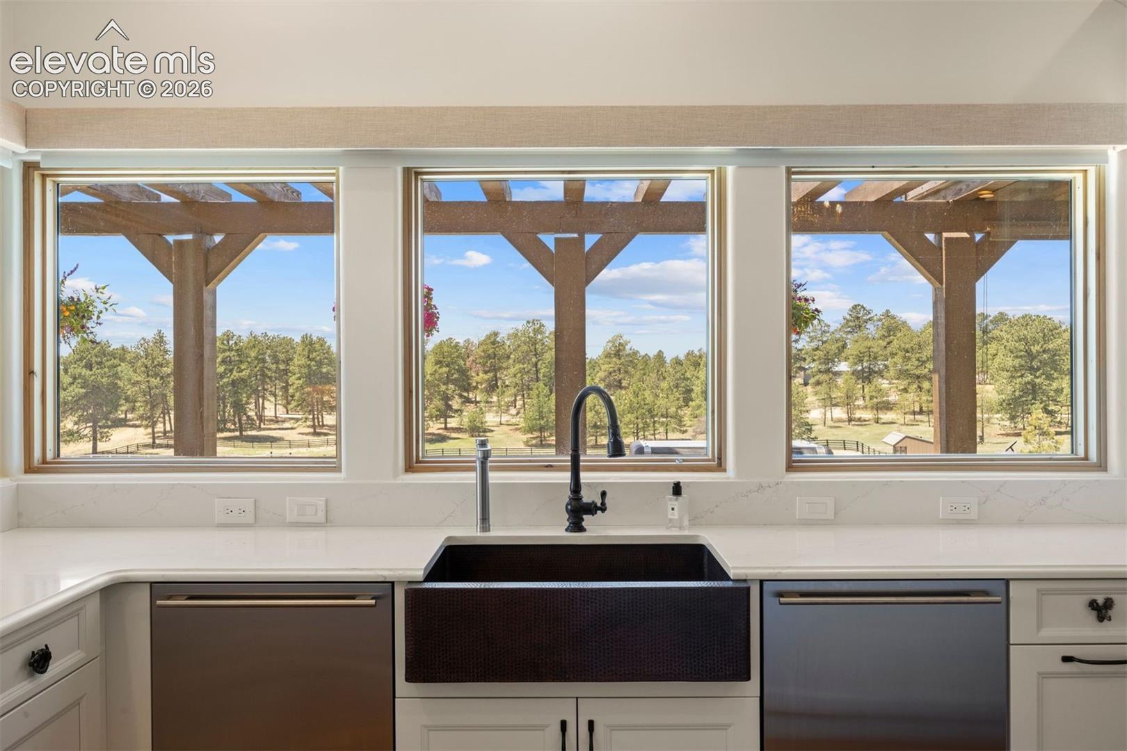 Wrap-around windows in the kitchen overlook the pergola, patio, pastures, and forest beyond, with electric, remote-controlled shades for effortless control. 
