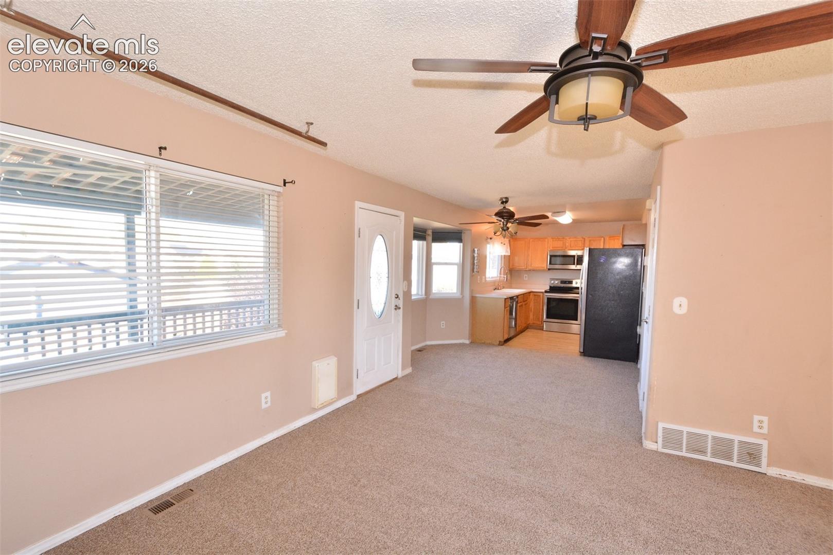 Open-concept living space featuring a ceiling fan, a kitchen with wood-finish cabinetry, stainless steel appliances, and a window with horizontal blinds