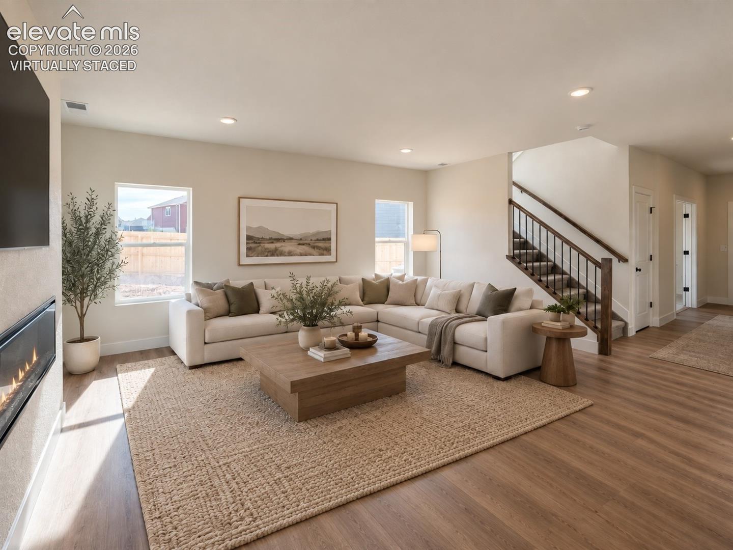 living room with sectional sofa, low wooden coffee table, textured area rug, and adjacent wood-and-iron staircase — virtually staged