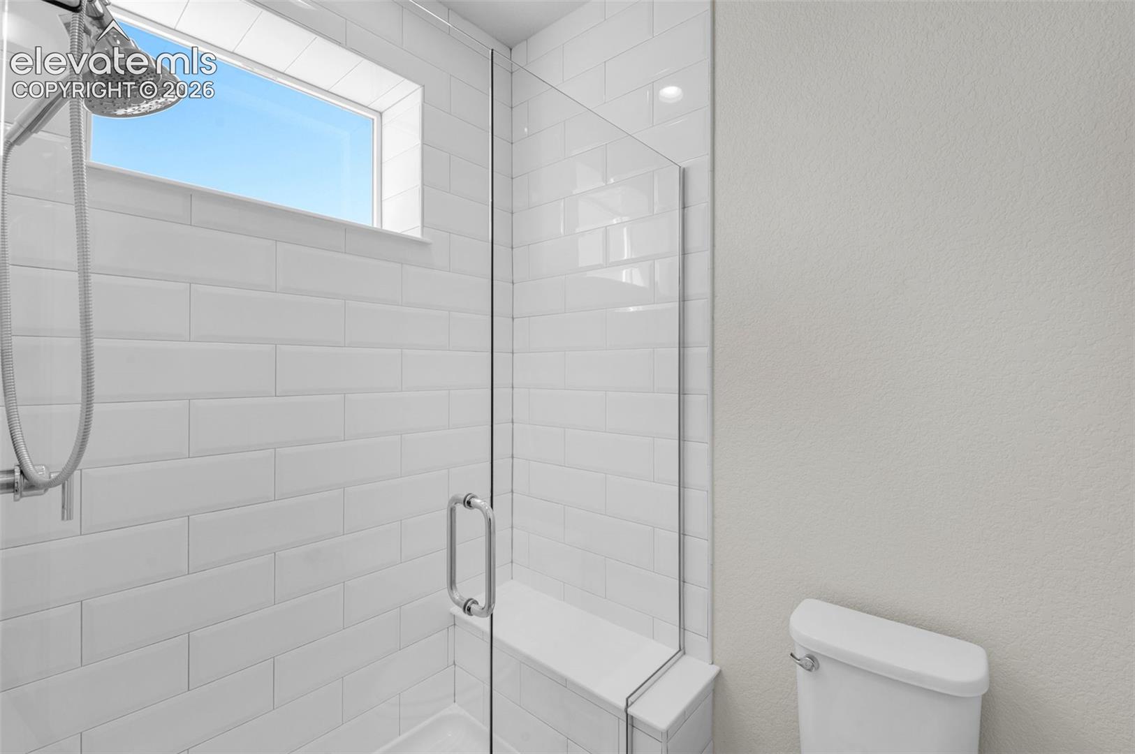 Shower featuring white subway tile, frameless glass enclosure, built-in tiled bench, polished chrome shower head, and an inset transom window