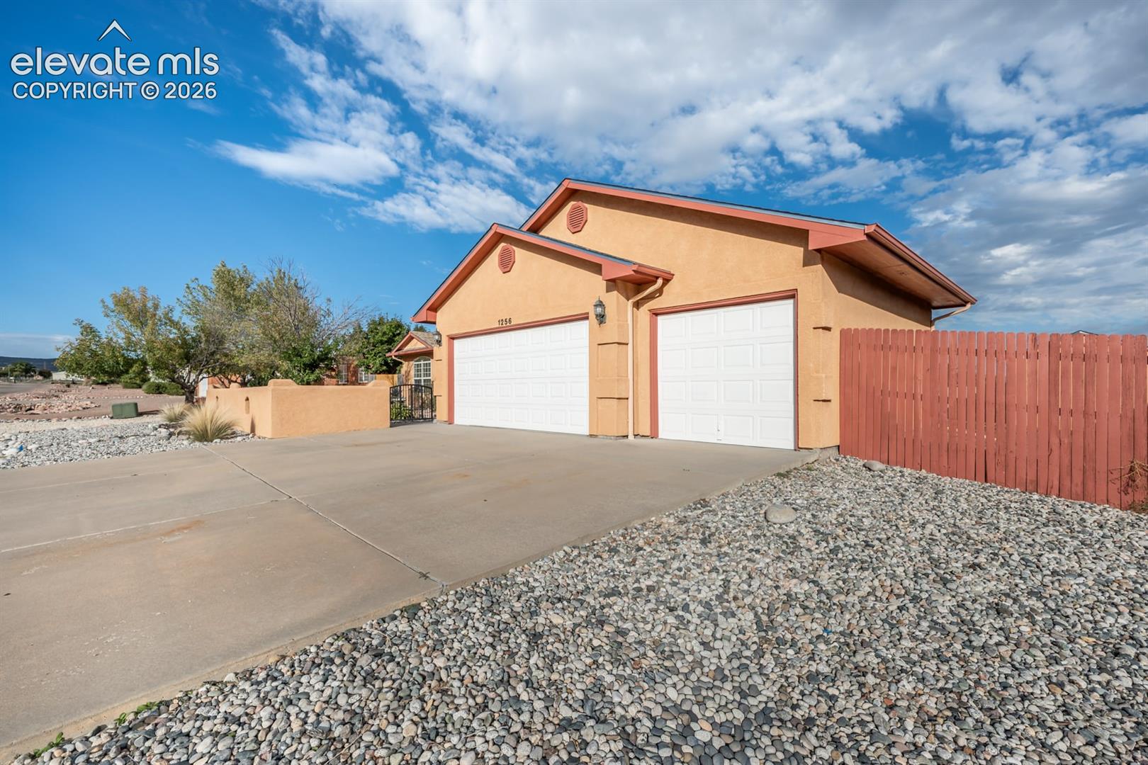 Stucco exterior residence featuring an attached two-car garage, concrete driveway, and red wood-style privacy fencing