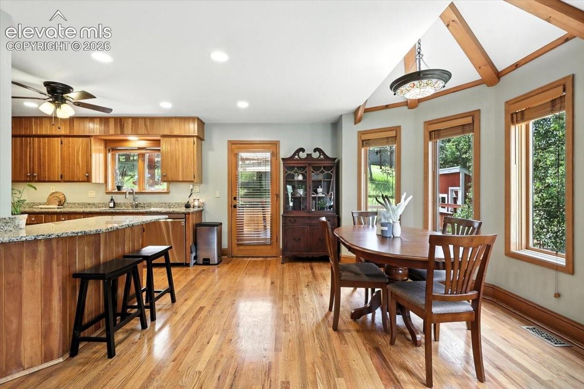 Kitchen featuring natural wood cabinetry, stone-surface countertops, wood-finish flooring, vaulted ceilings with exposed beams, and multiple windows