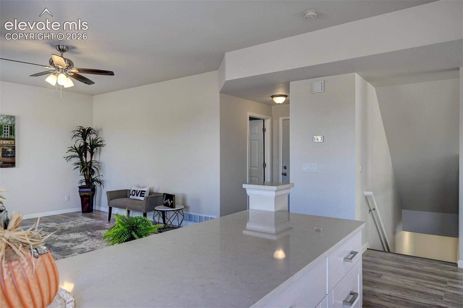 Kitchen island with quartz countertop and white cabinetry, wood-finish flooring, and ceiling fan with integrated lighting