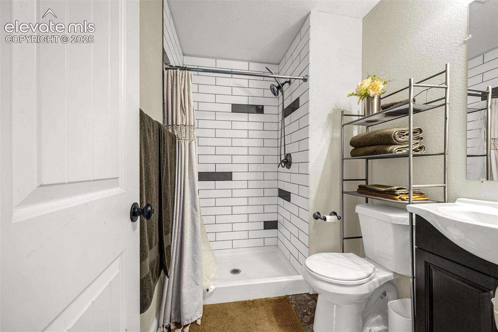 Full-height shower featuring white subway tile walls with black accent tiles, a showerhead with matte black finish, and a dark-toned vanity cabinet