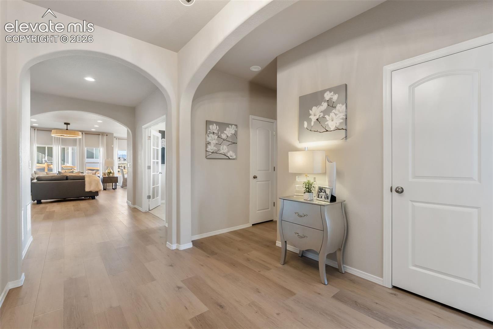 Interior hallway featuring arched architectural entryways, light-toned wood-finish flooring, recessed lighting, and white paneled doors
