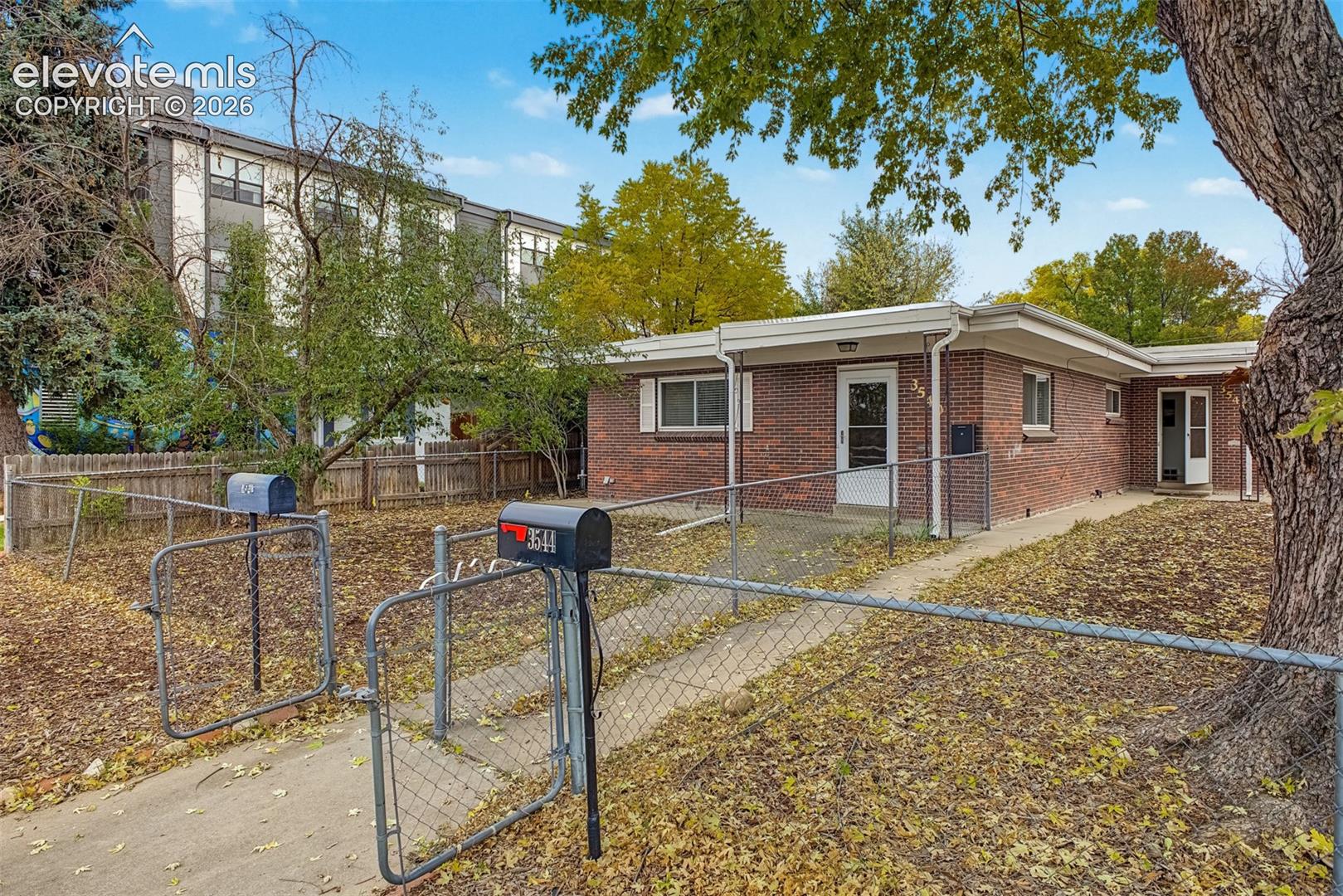 Single-story brick exterior featuring a flat roofline, concrete walkway, and chain-link perimeter fencing