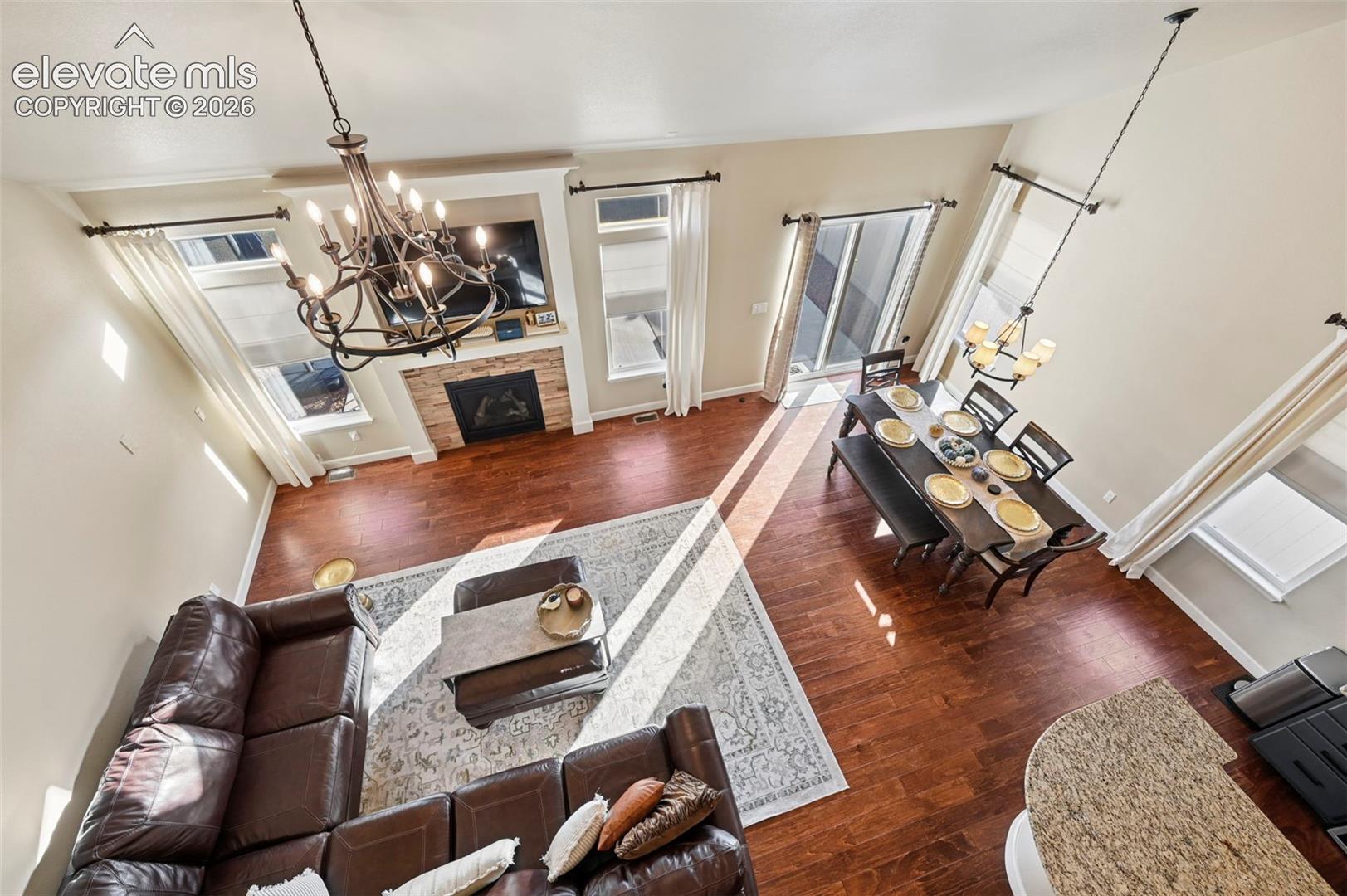 High ceilings with a decorative chandelier, wood-finish flooring, a stone-clad fireplace, and sliding glass doors to outdoor access