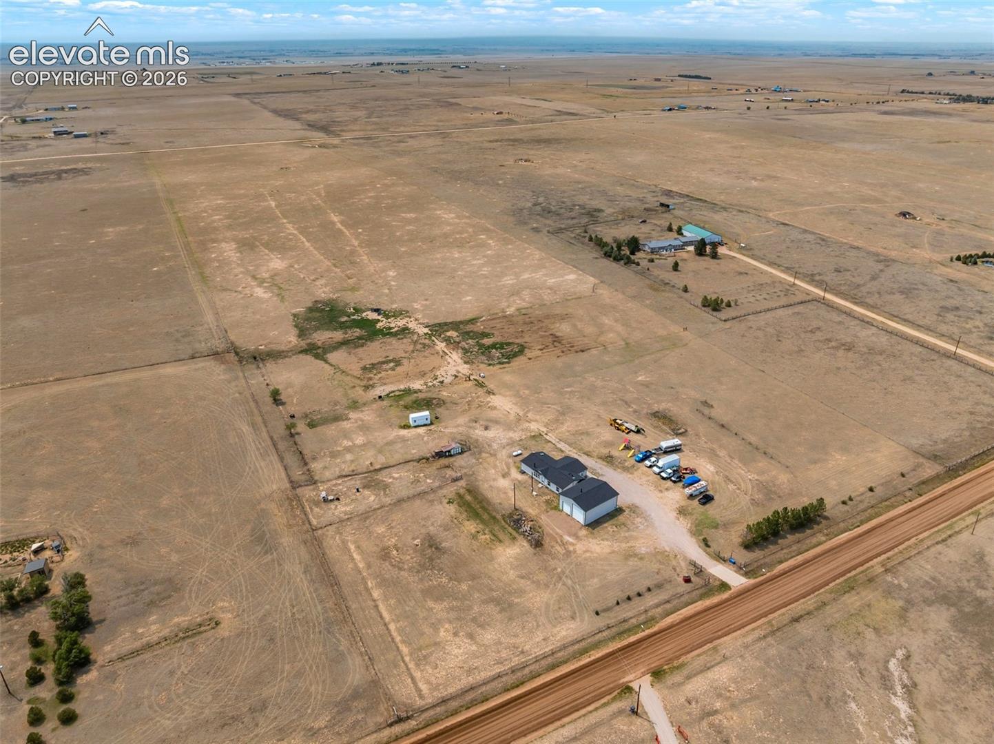 Expansive rural property featuring multiple structures, including a two-story residence with an attached garage, an additional outbuilding, and a second distant structure with a light-colored roof