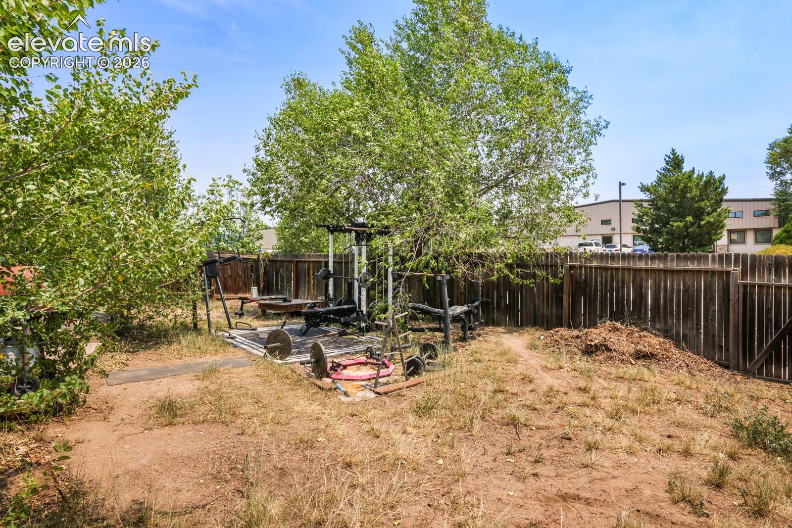 Fenced backyard featuring mature trees and a dedicated paved area