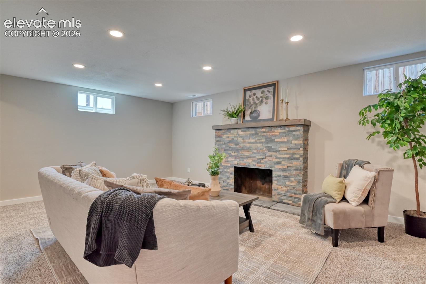 Recessed ceiling lighting, stone-clad fireplace with wood mantle, and light-toned wall finishes