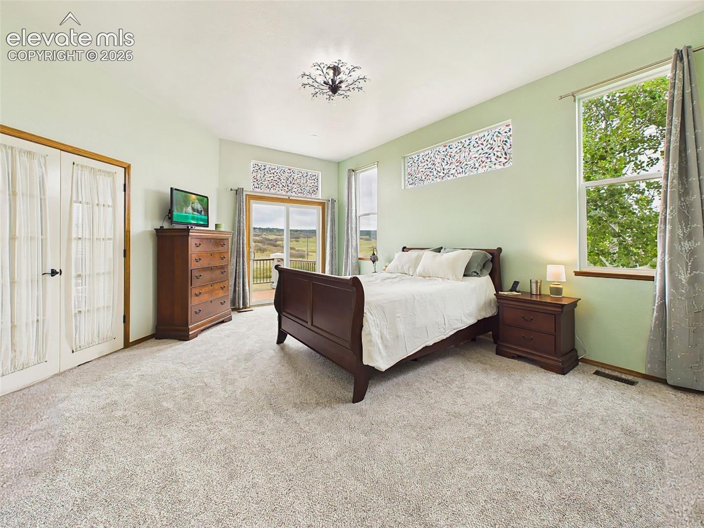 Spacious primary suite featuring plush carpeting, large windows, and private deck access with scenic surrounding views.