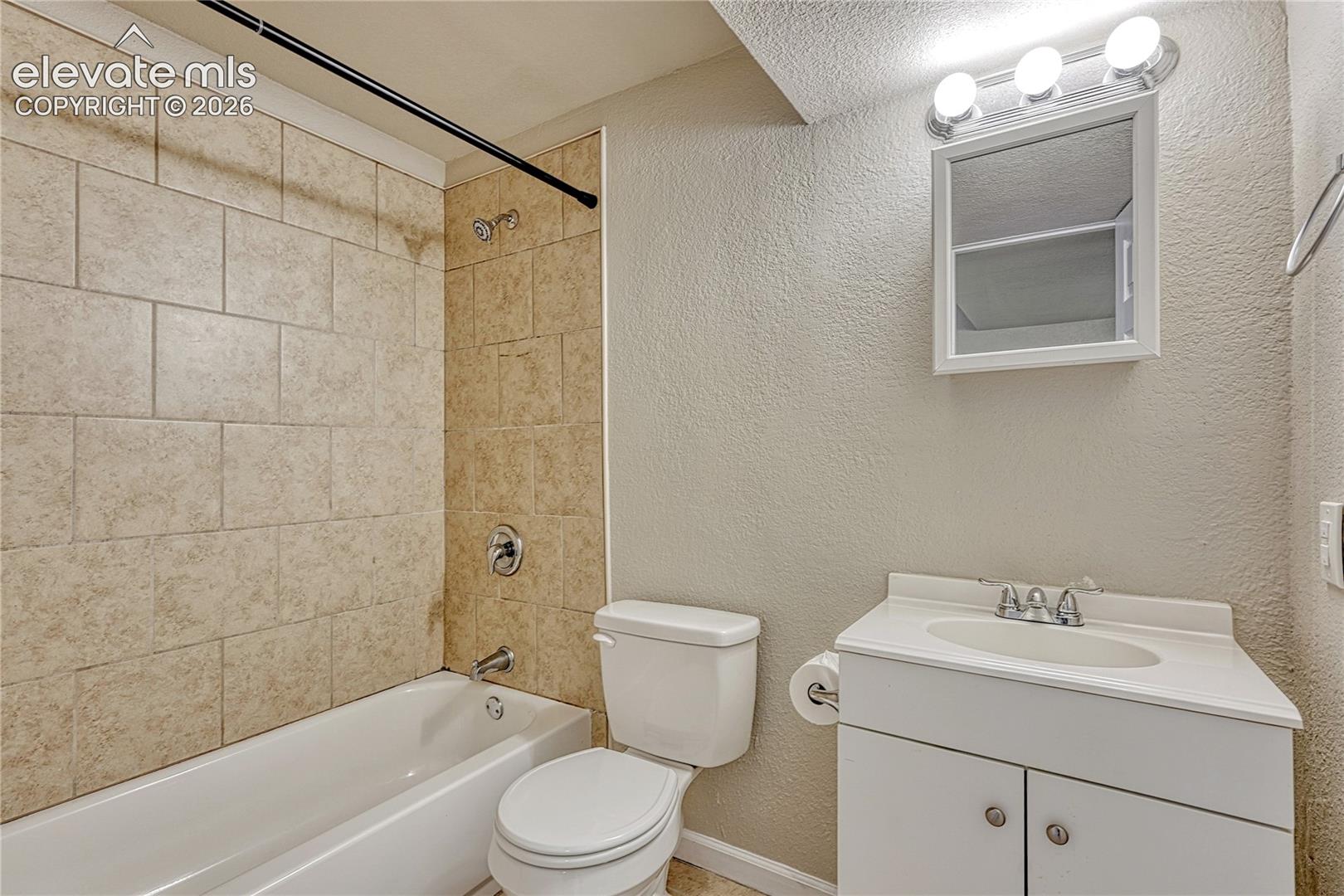 Bathroom featuring a tub and shower combination with neutral-toned wall tile, a white vanity with an integrated sink, and a wall-mounted mirrored cabinet with integrated lighting