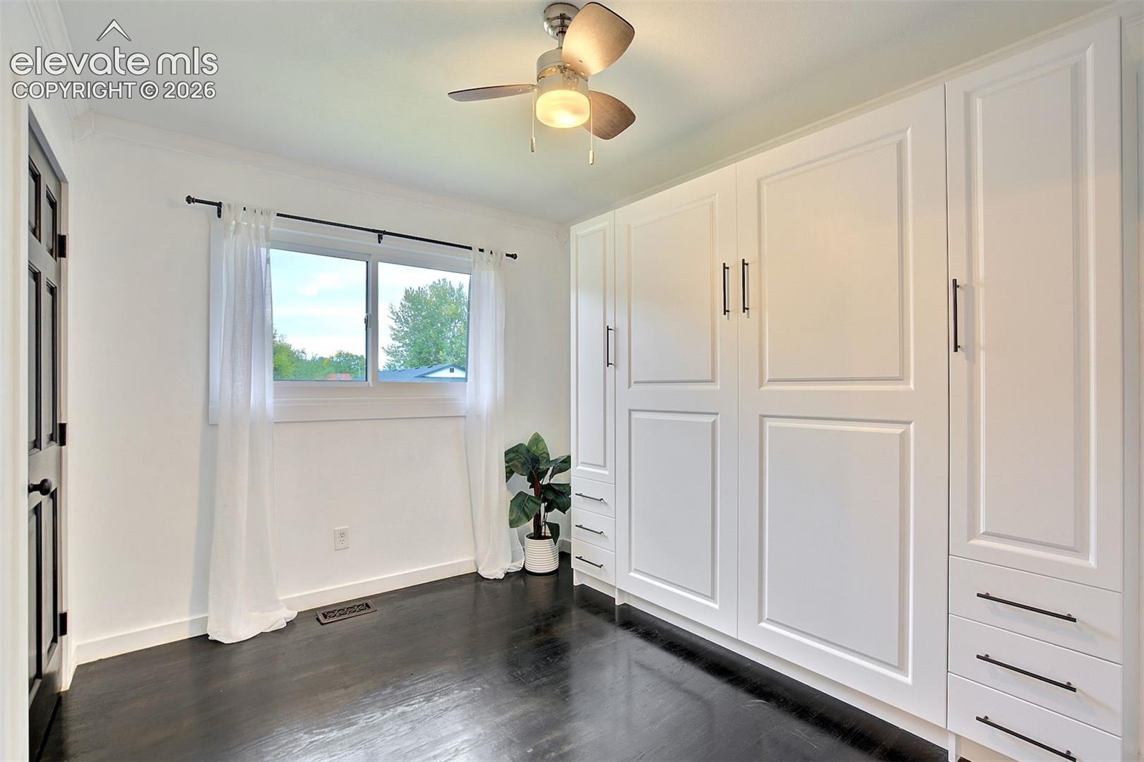 Custom white built-in cabinetry featuring integrated storage, wood-finish flooring, sliding window, and ceiling-mounted light fixture