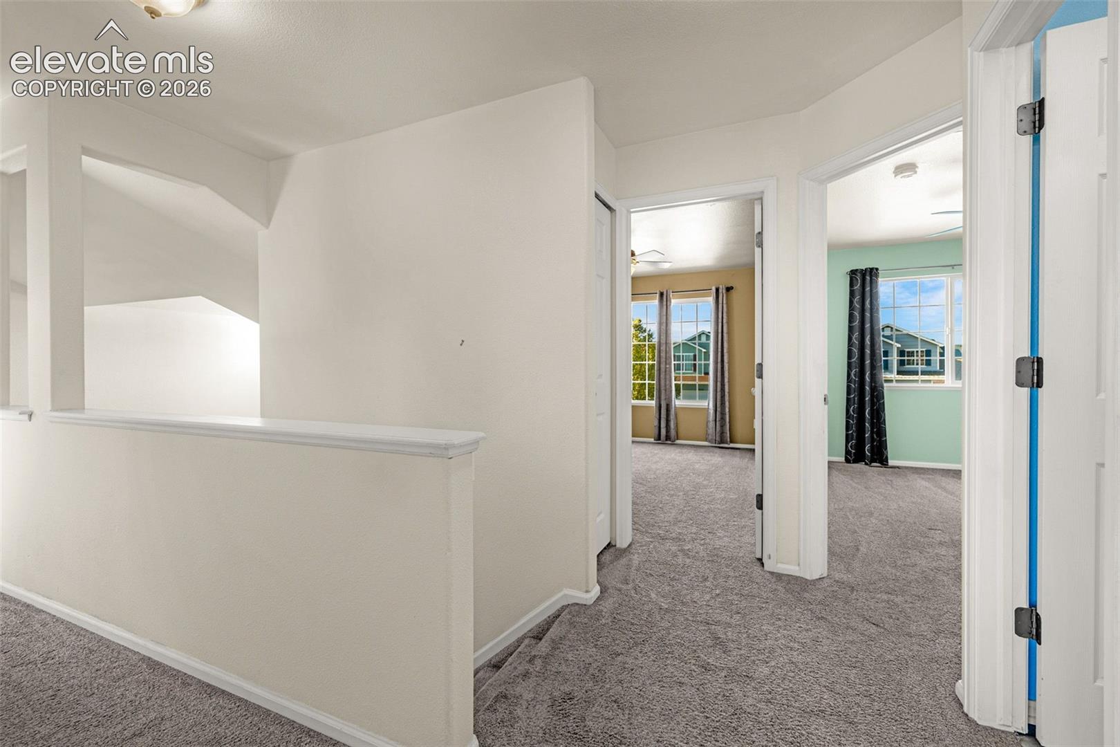 Hallway featuring neutral-toned carpeting, white interior doors, and a partial height wall with a cap