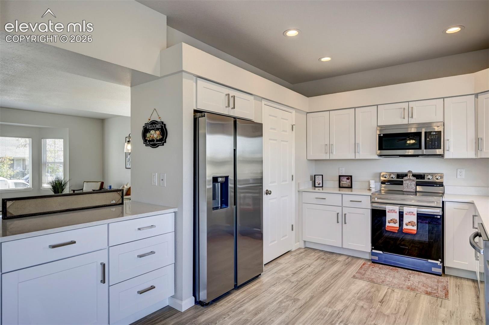 Kitchen featuring white shaker-style cabinetry, stainless steel appliances, light-toned stone countertops, and wood-finish flooring