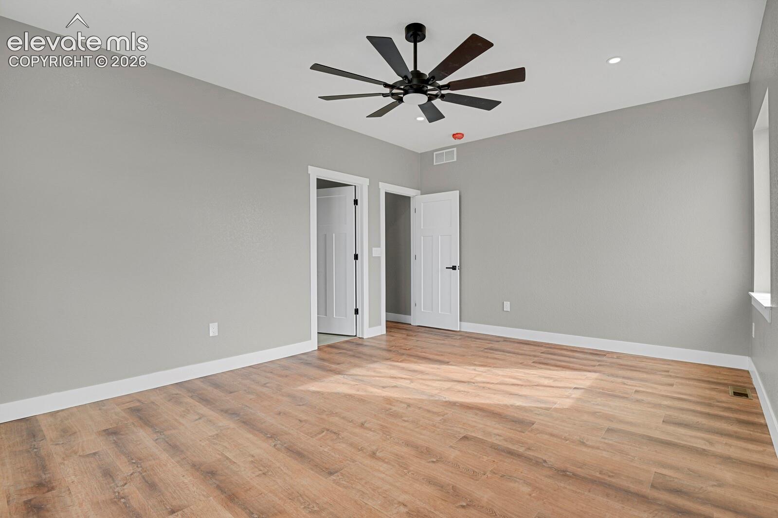 Neutral-toned interior space featuring wood-finish flooring, a multi-blade ceiling fan, recessed lighting, and multi-panel interior doors with matte black hardware