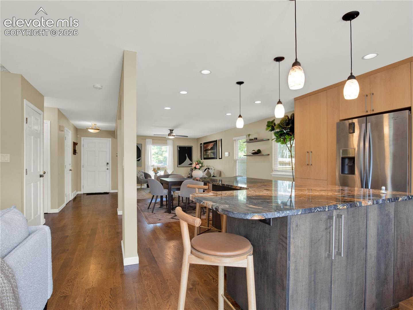 Kitchen featuring a stone-surface island, wood-finish flooring, custom flat-panel cabinetry, stainless steel refrigerator, and recessed lighting