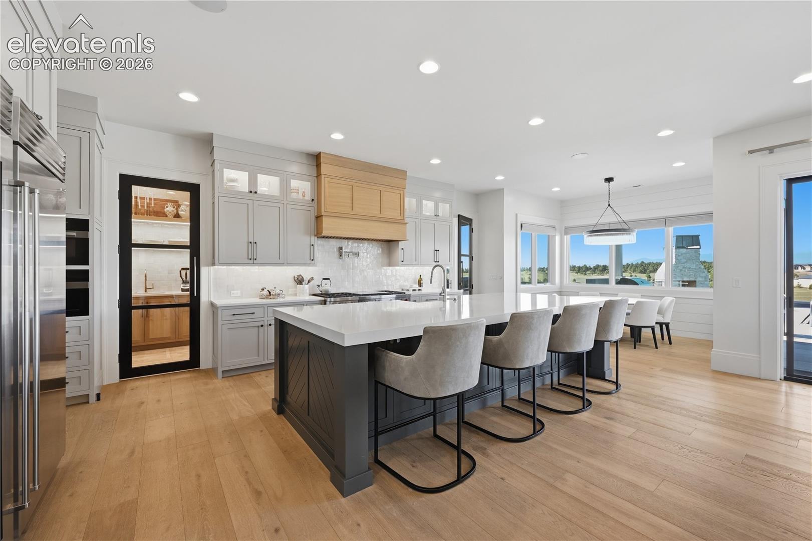 Gourmet kitchen featuring a large center island, custom cabinetry, wood-finish flooring, a stainless steel refrigerator, and a pantry with a glass-paneled door