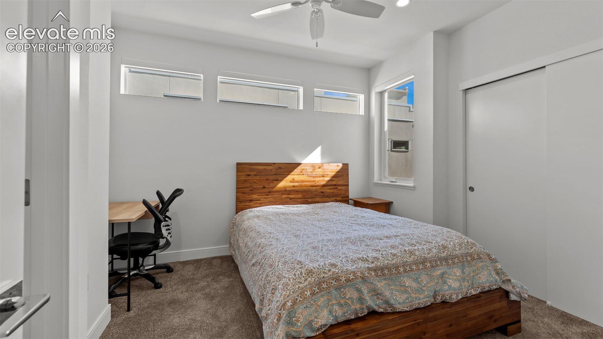 Bedroom featuring neutral carpeting, three horizontal clerestory windows, a vertical window, and a ceiling fan