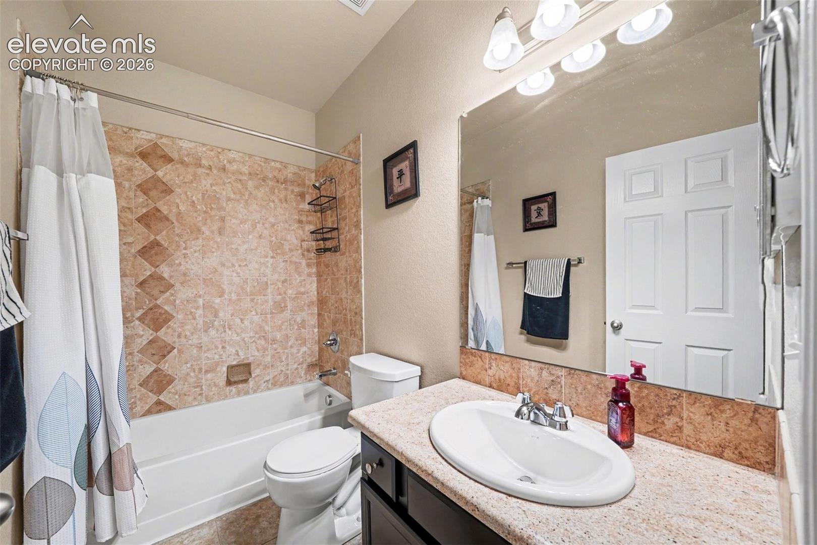 Bathroom featuring a combination shower and tub with patterned tile surround, a single vanity with an oval basin, a large wall-mounted mirror, and a toilet