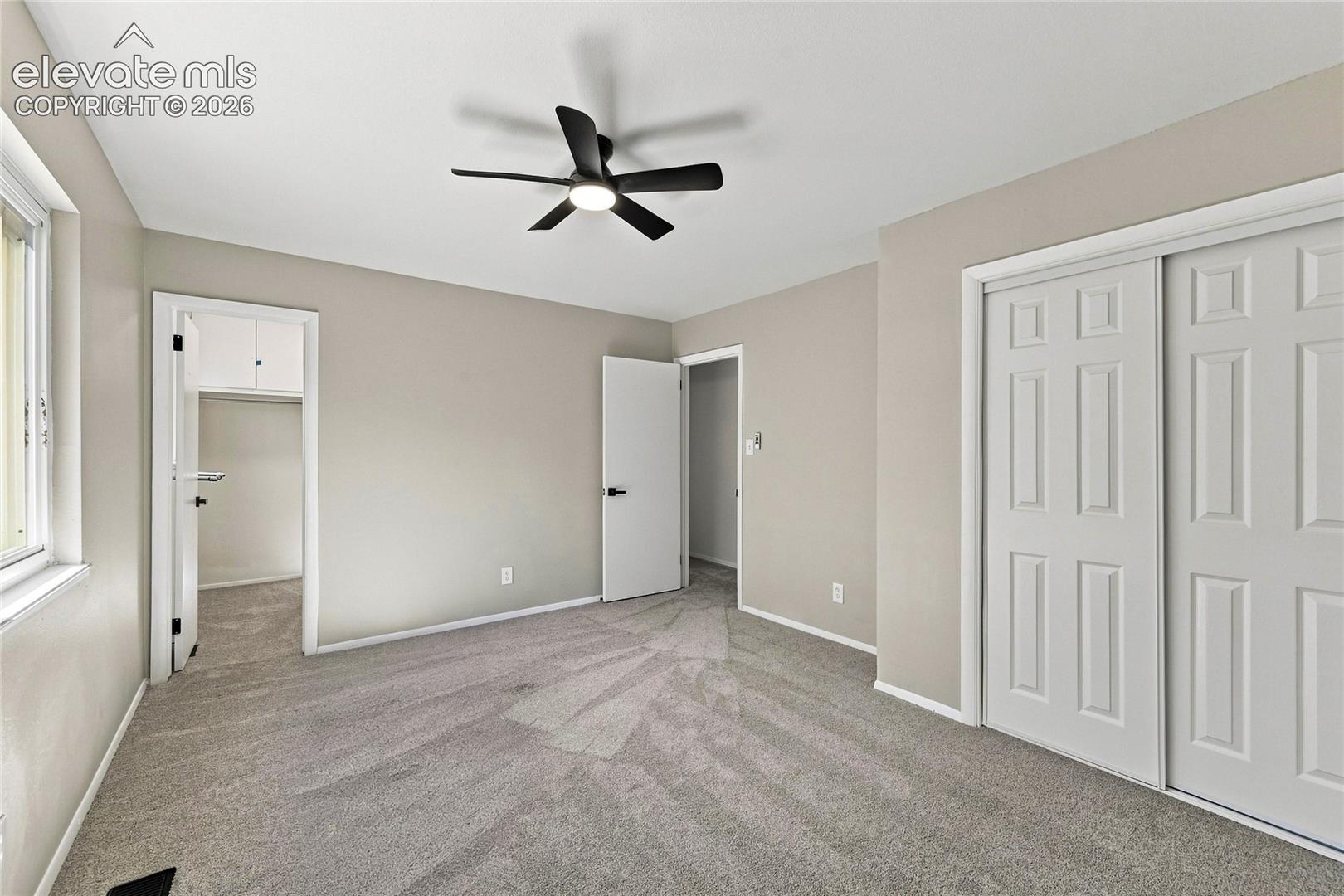 Recessed window, ceiling fan with integrated lighting, neutral wall paint, gray carpeting, and white paneled bi-fold closet doors