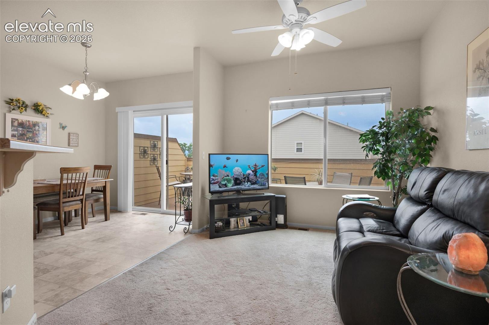 Open-concept living area featuring a ceiling fan with integrated lighting, a large window, and light-toned carpeting