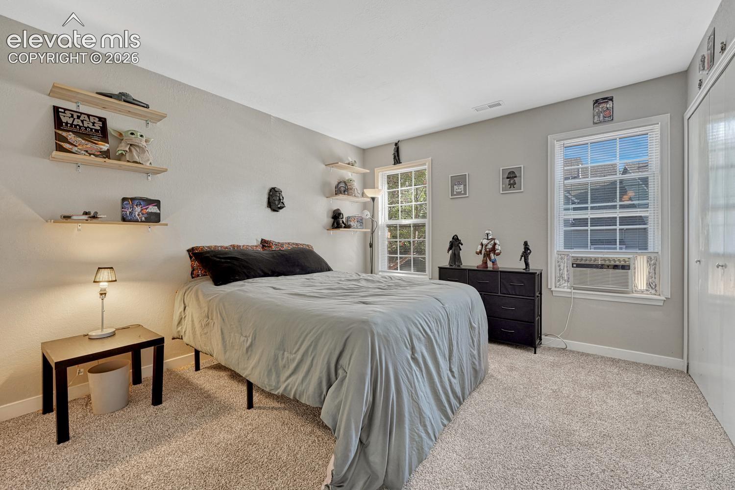 Neutral-toned carpeting, two windows with white trim, built-in shelving, and a closet with bifold doors & white barn door to primary bathroom