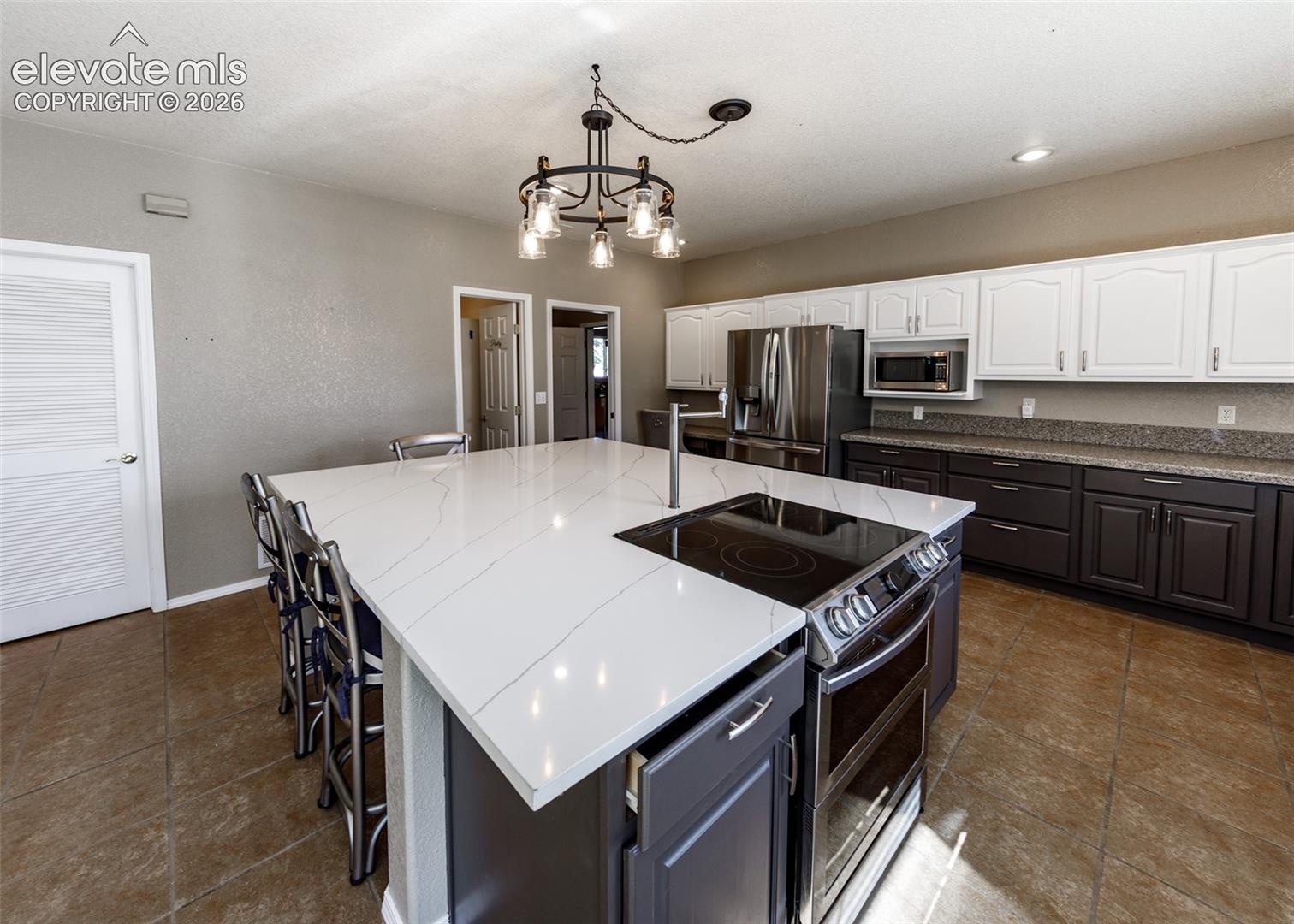 Kitchen featuring a large central island with a stone-composite countertop, two-toned cabinetry, stainless steel built-in appliances, and a modern tiered chandelier
