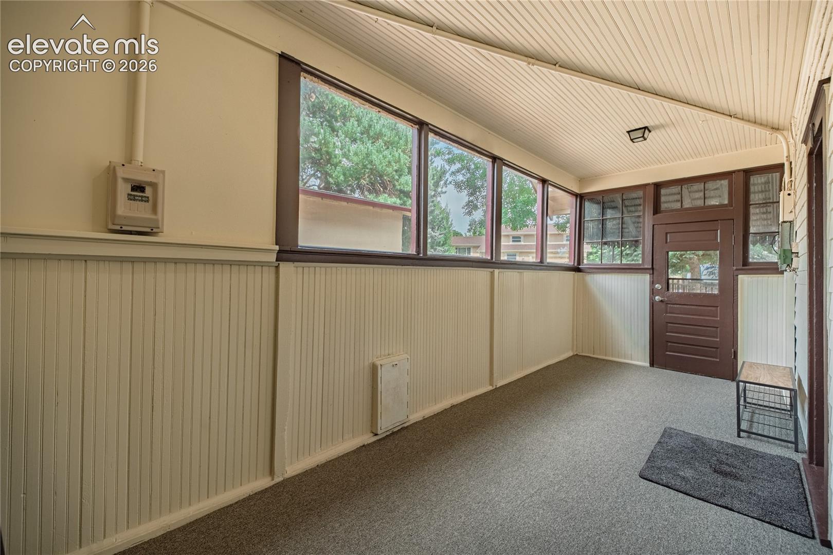 Enclosed porch featuring multiple windows, paneled walls, and a wood-panel door