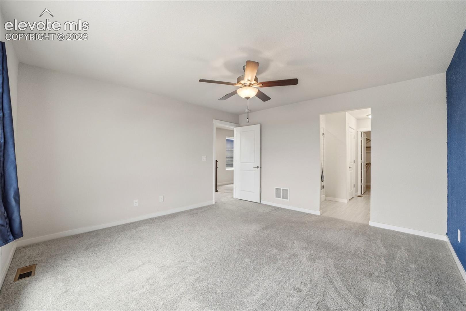 Spacious room with light gray carpeting, a ceiling fan with light fixture, and a contrasting accent wall