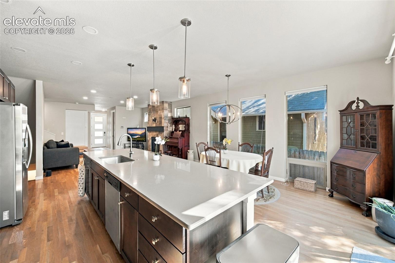 Kitchen featuring a large island with a quartz countertop, dark-finish cabinetry, recessed lighting, pendant light fixtures, and wood flooring. Staircase access to unfinished basement
