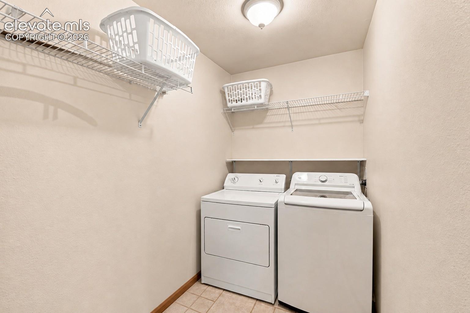 Laundry area featuring a tile floor, white appliances, overhead lighting, and two wire storage shelves