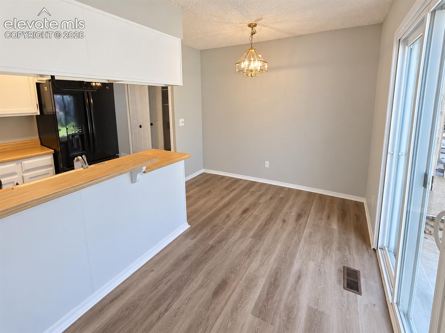 Dining area featuring wood-finish flooring, a metal geometric pendant light fixture, a pass-through kitchen counter with a wood surface, and sliding glass doors