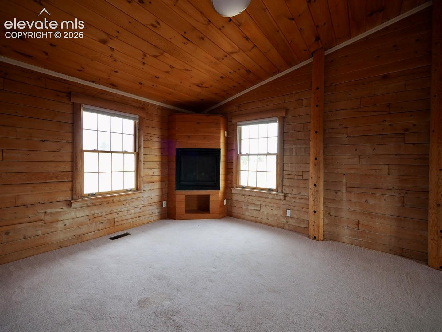 Interior featuring natural wood-plank walls and ceiling, vaulted roofline, built-in corner fireplace, and two-over-two grid windows