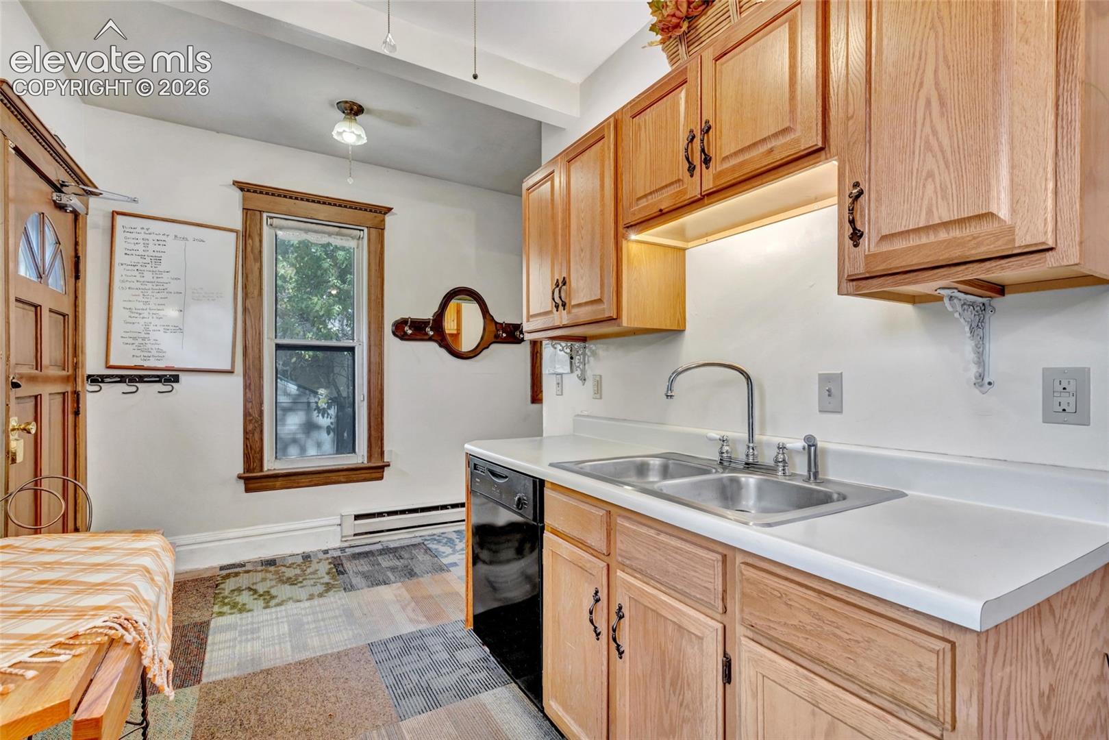 Kitchen featuring light wood cabinetry, white countertops, double-basin stainless steel sink with high-arch faucet, and a window with wood trim