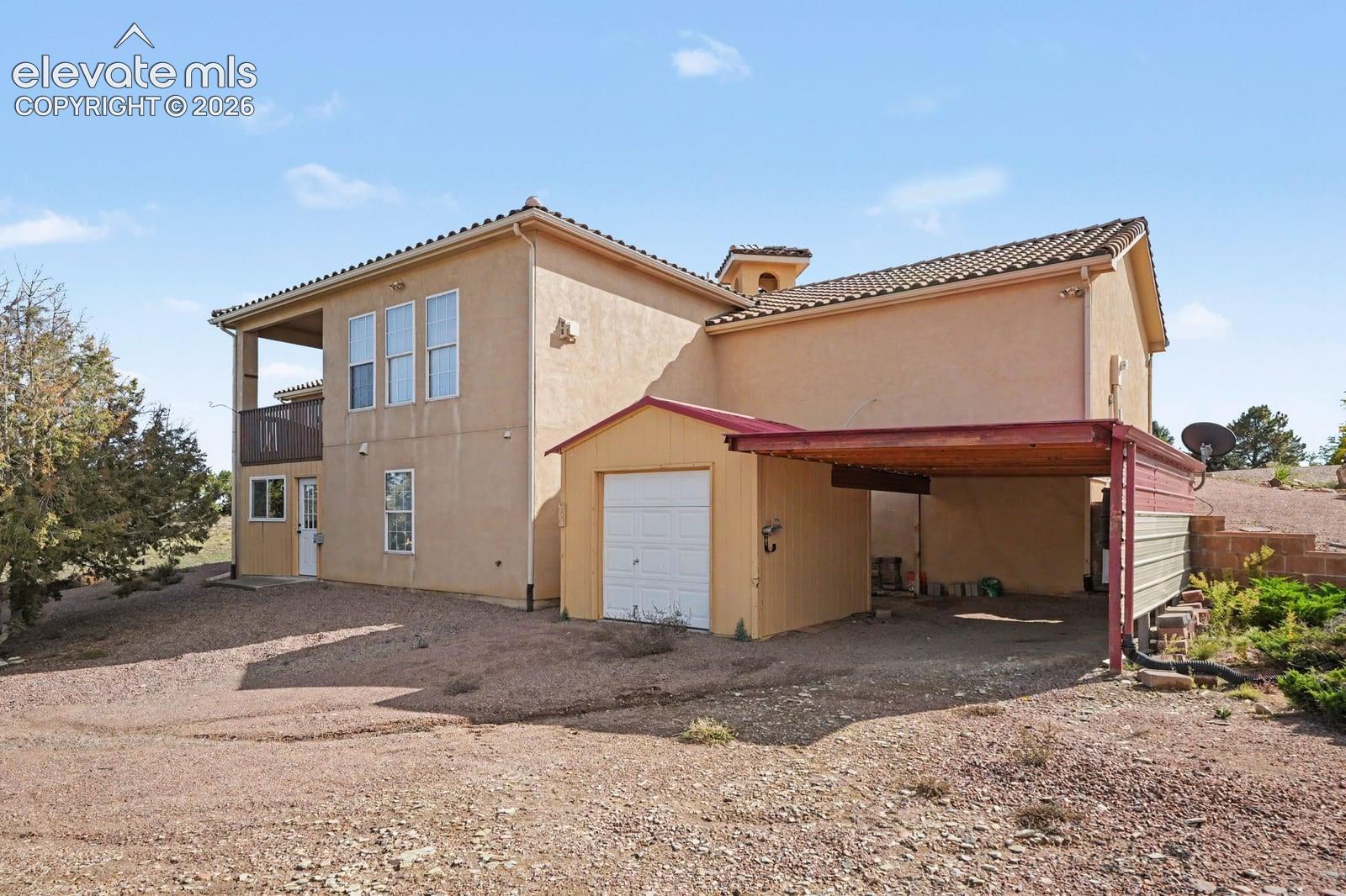 Stucco exterior residence featuring a tile roof, covered balcony, detached single-car garage, and an attached carport