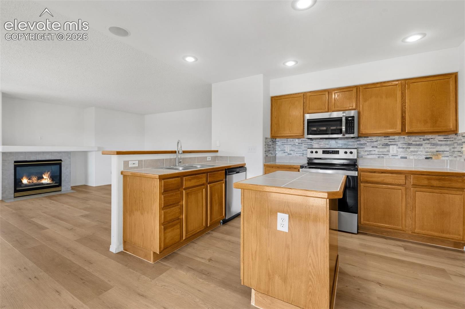 Kitchen with wood-finish flooring, recessed lighting, wood cabinetry, stainless steel appliances, and a tile backsplash