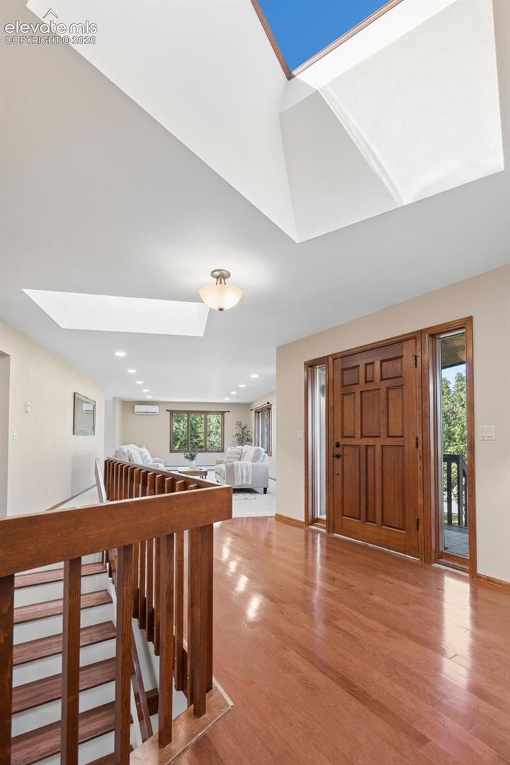 Hardwood flooring throughout, a paneled wood entry door, and multiple skylights