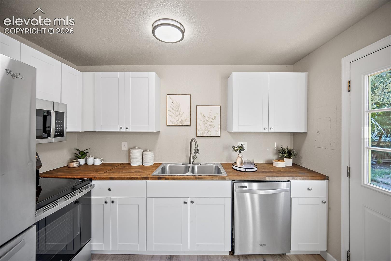 White shaker cabinetry, wood-finish countertops, stainless steel appliances, double basin sink, and ceiling-mounted flush lighting