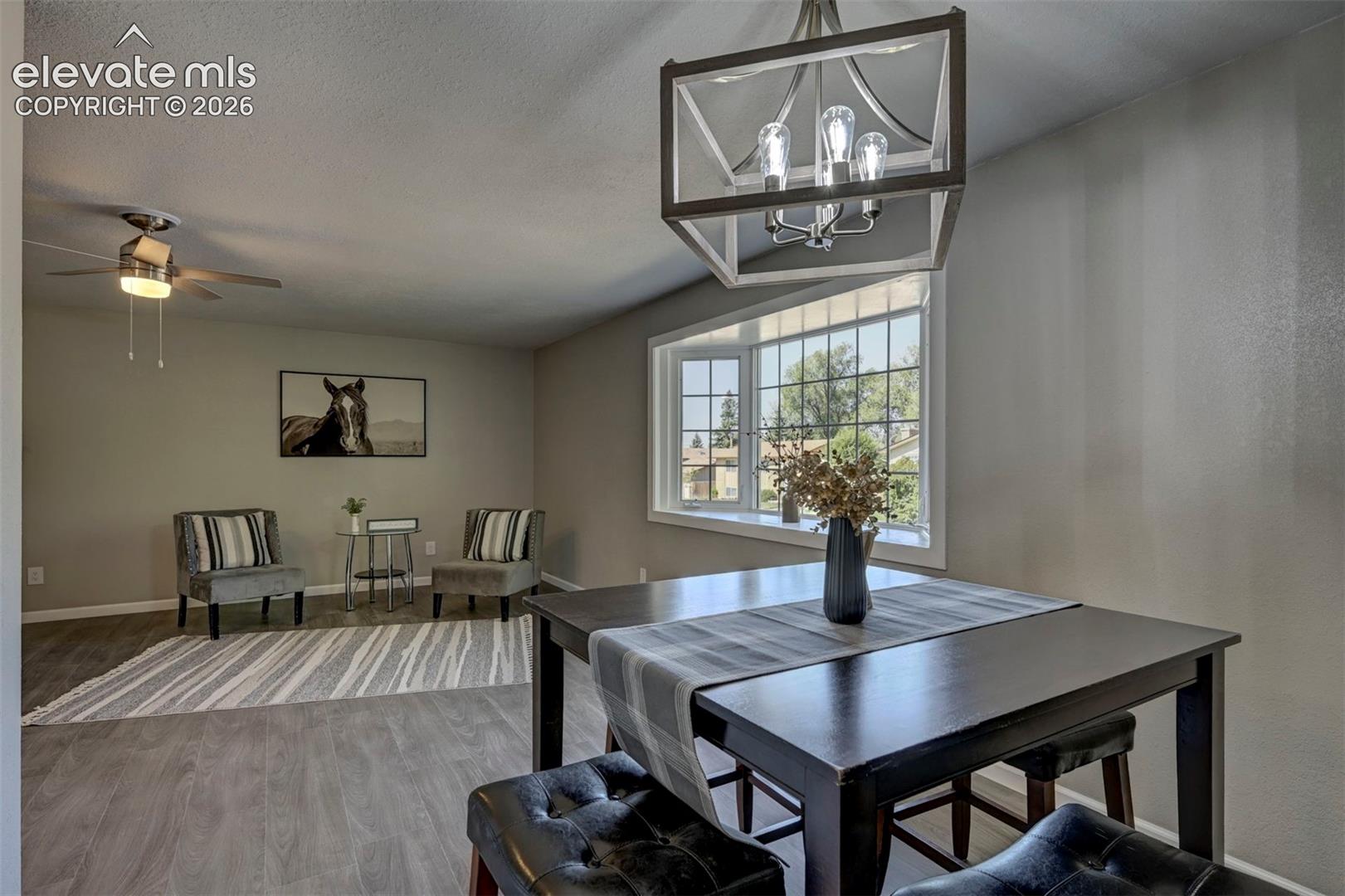 Open concept interior featuring wood-finish flooring, a geometric metal-frame chandelier, a large bay window, and a ceiling-mounted light fixture with a fan