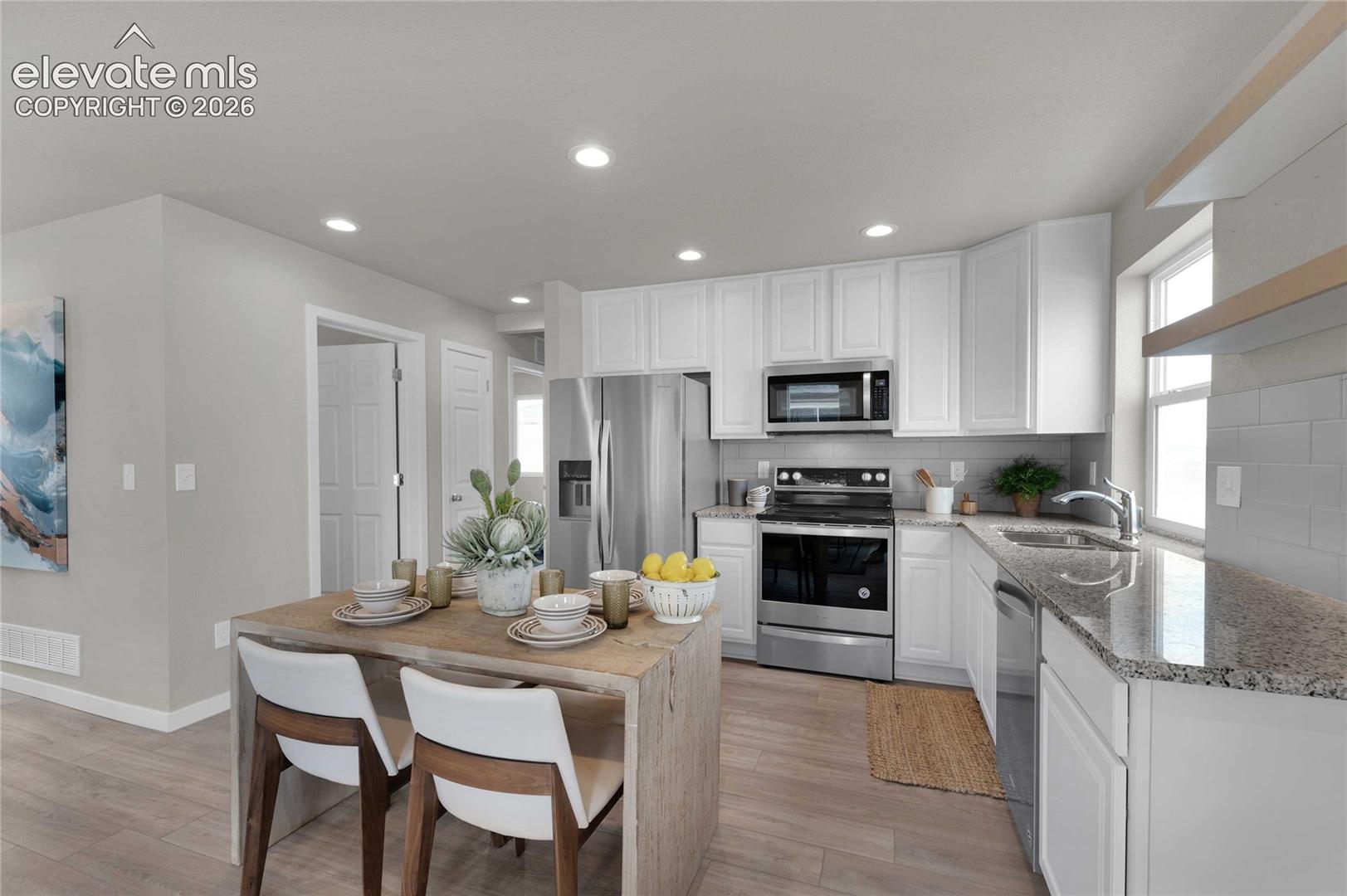 Kitchen featuring wood-finish flooring, white cabinetry, stainless steel appliances, granite countertops, and subway tile backsplash
*photos of a model home*