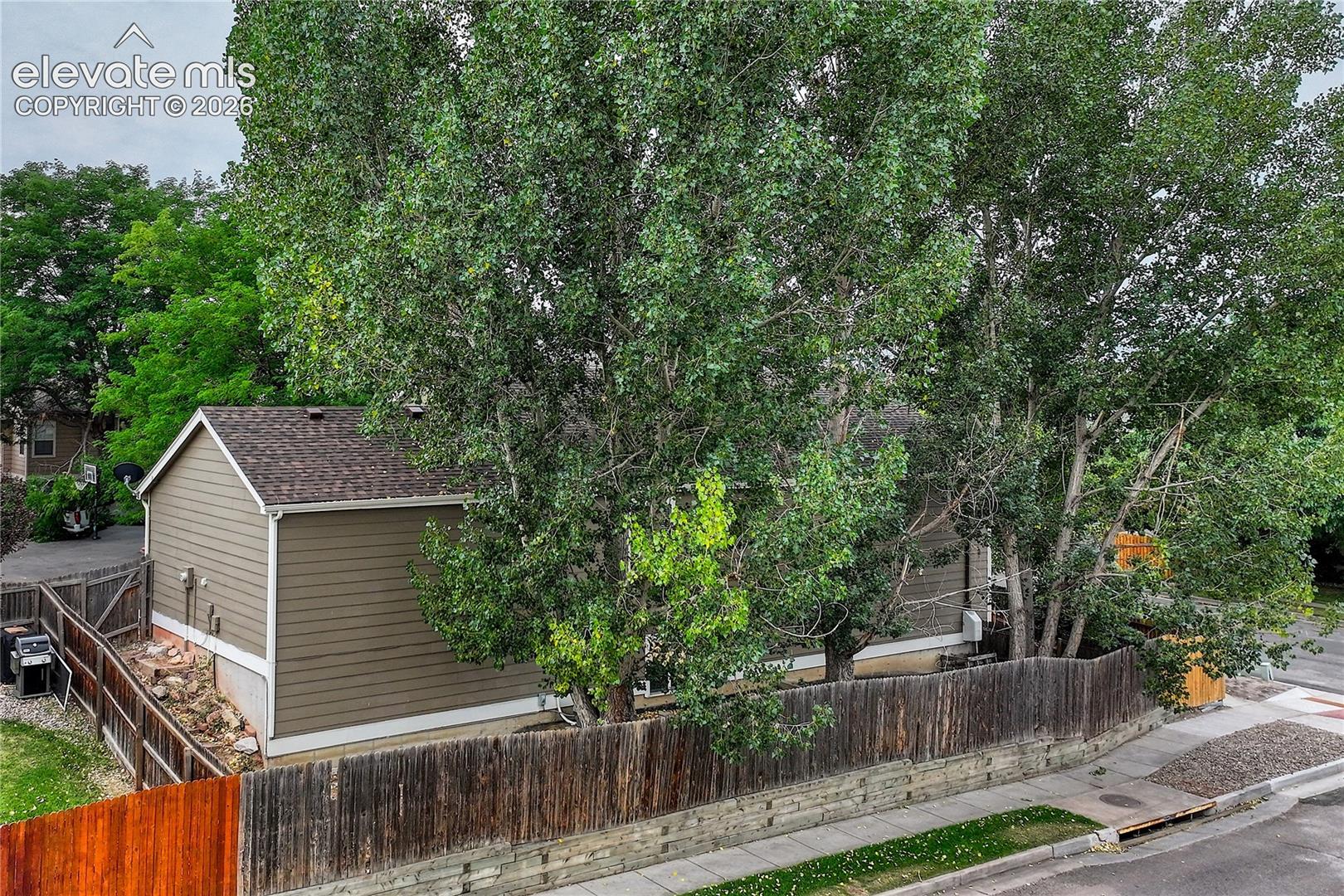 Horizontal siding exterior with a shingled roof, enclosed by a wood privacy fence and mature trees