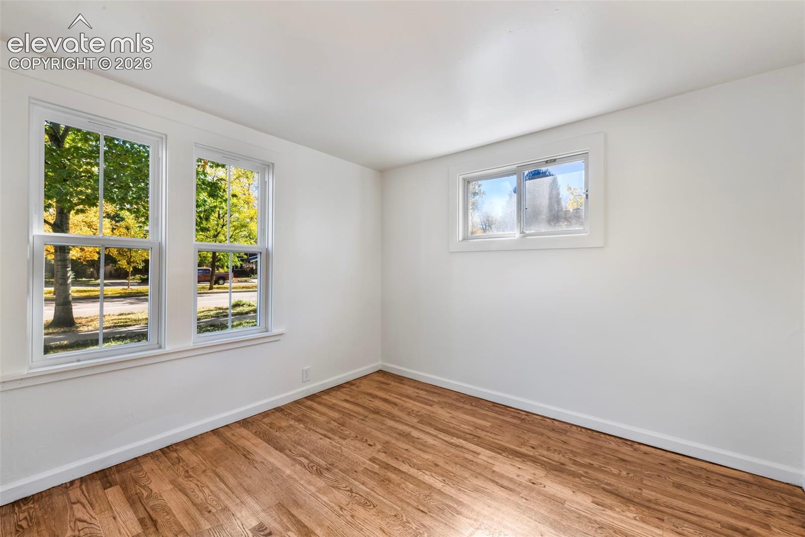 Room featuring wood-finish flooring, white walls, double-hung windows, and a sliding window