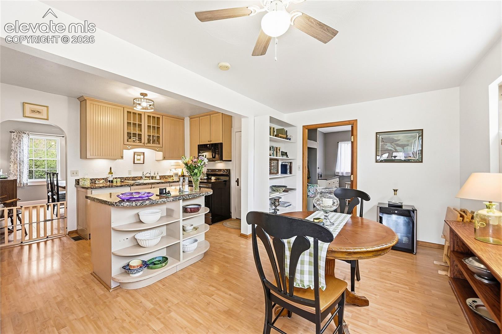 Kitchen featuring light-wood cabinetry, stone-finish countertops, a built-in island with integrated curved shelving, wood-finish flooring, and a ceiling fan