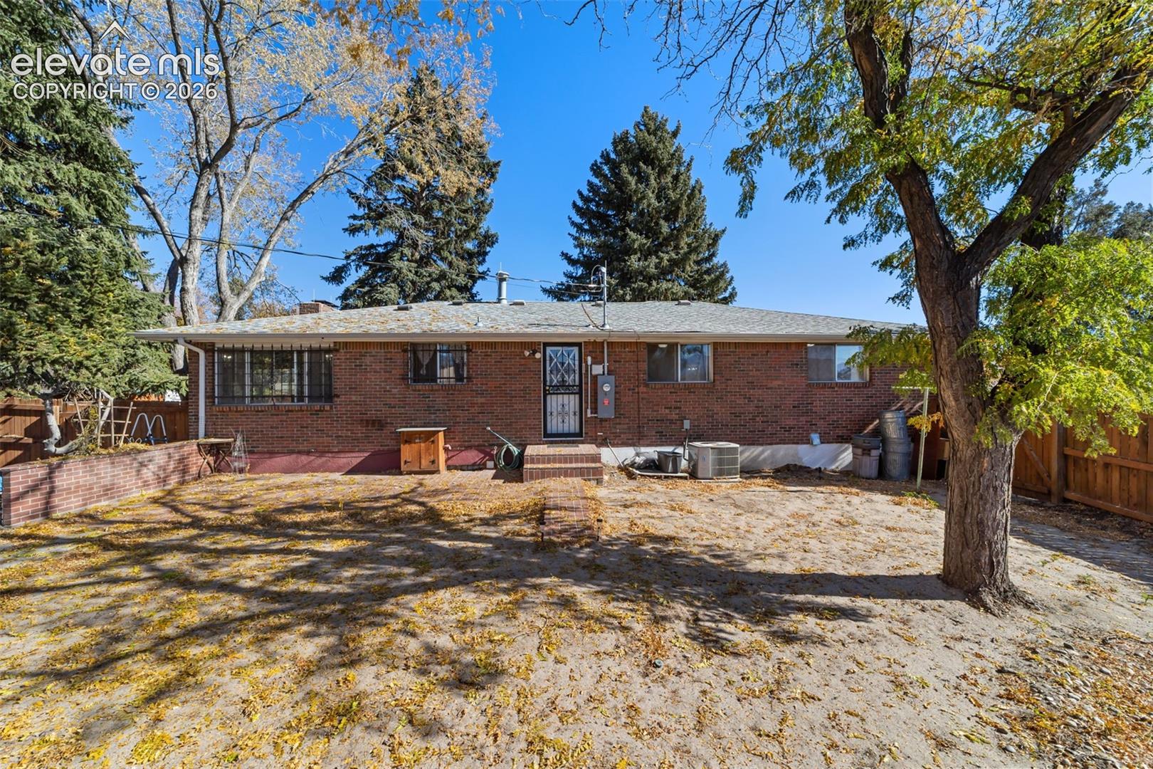Expansive backyard with a full brick exterior, a mature deciduous tree, and a partial wood fence