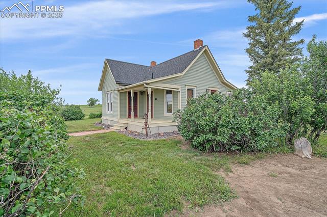 View of side of property with a porch, a yard, a shingled roof, and a chimney