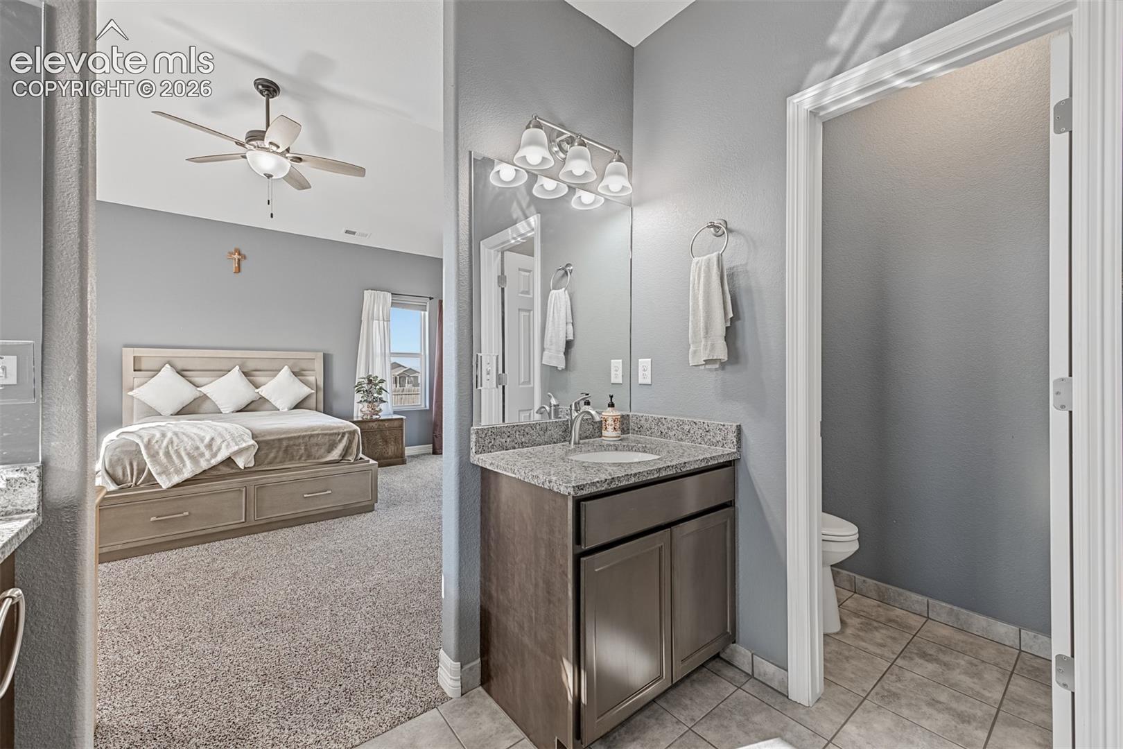 Walk-in shower with dark tile surround and stone flooring, stone-topped dual vanities vanity with undermount sinks and a walk-in closet. 