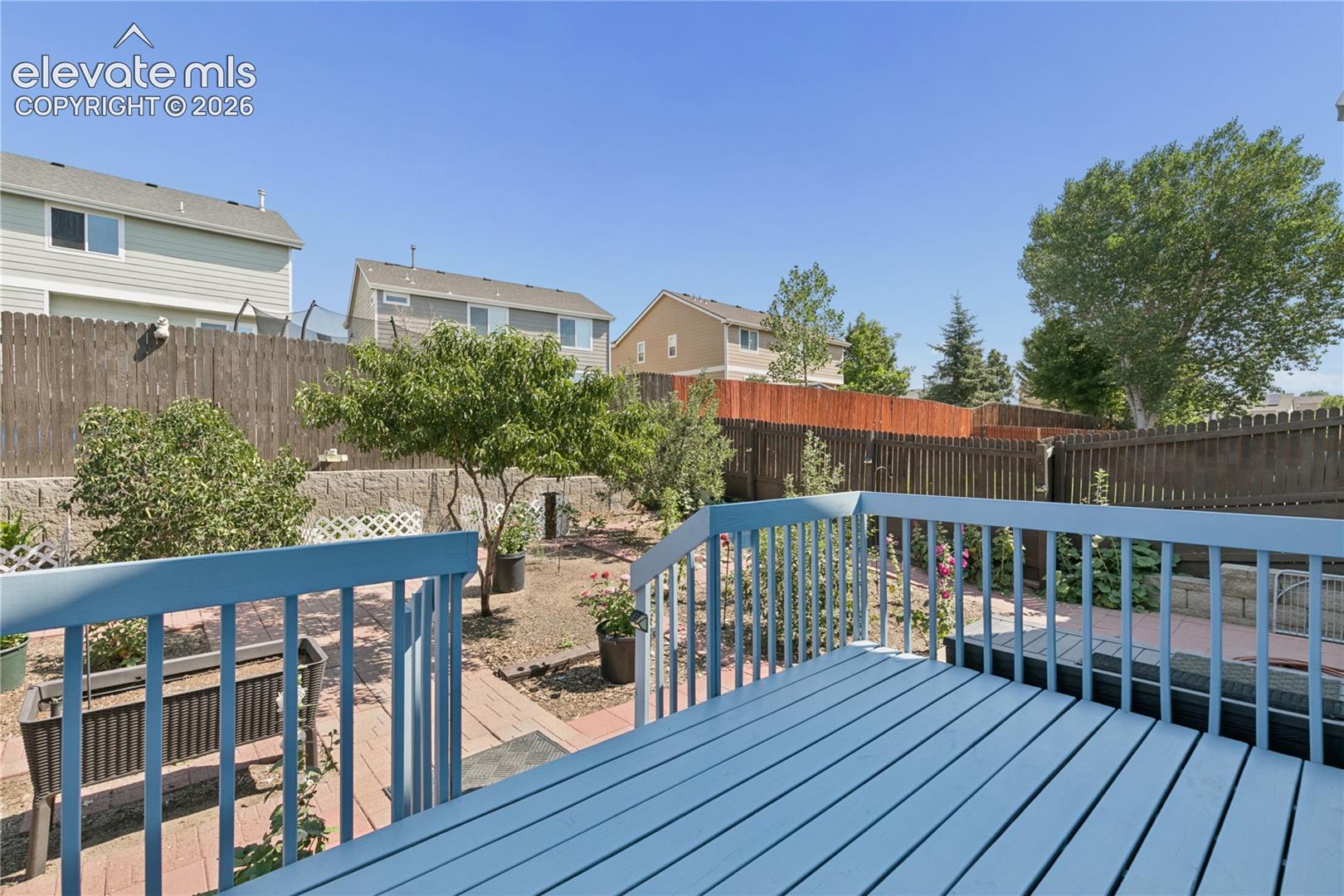 Expansive outdoor deck with painted wood planks, leading to a backyard featuring brick pavers, a retaining wall, and mature trees