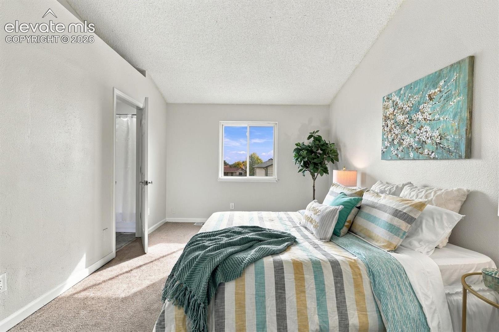 Neutral-toned bedroom featuring vaulted ceilings, carpeting, and a sliding window