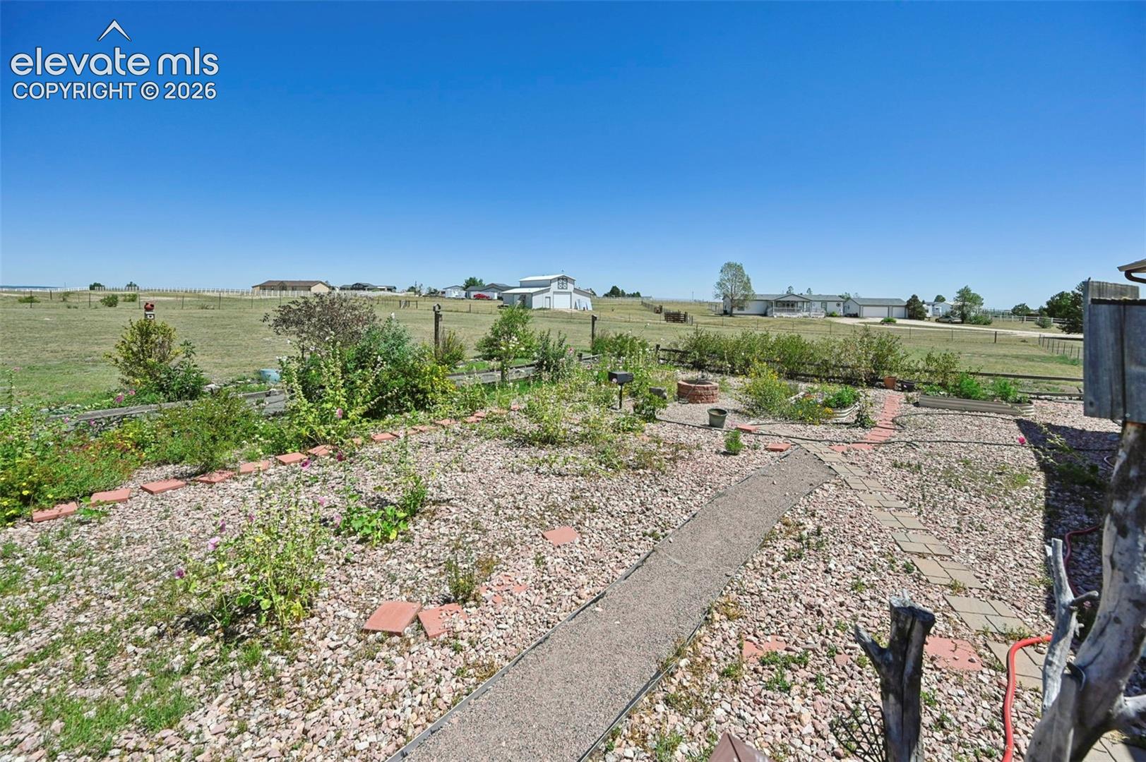 Expansive backyard featuring a gravel landscape, brick-lined garden beds, and a stone pathway